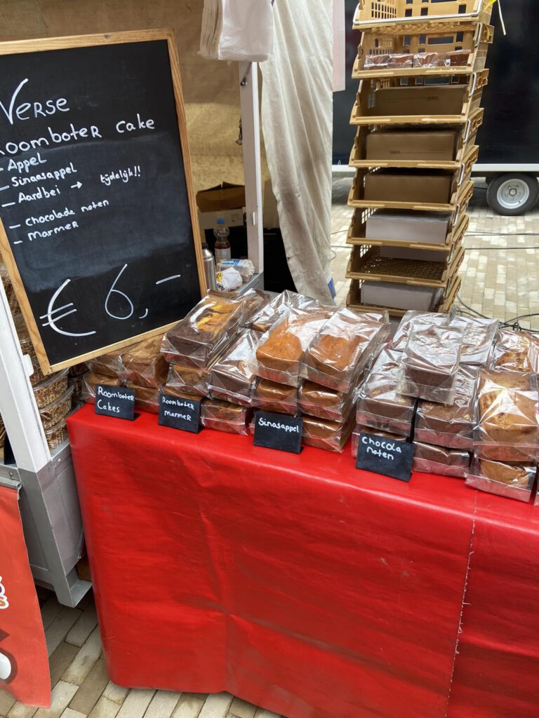Verschillende smaken ambachtelijke roomboter cakes gepresenteerd op een markttafel bij De Vries.