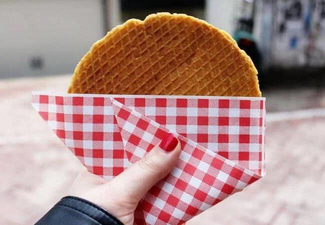 Een close-up van een verse, warme stroopwafel in een herkenbaar rood-wit geblokt zakje.